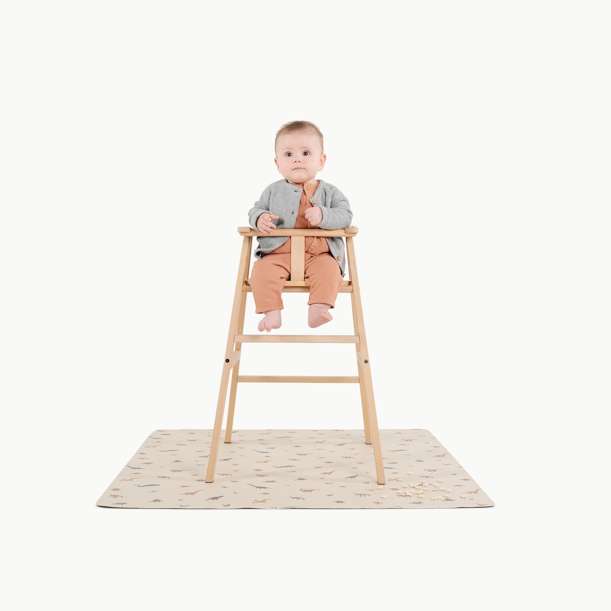 Dinosauria@baby in a high chair on a mini mat