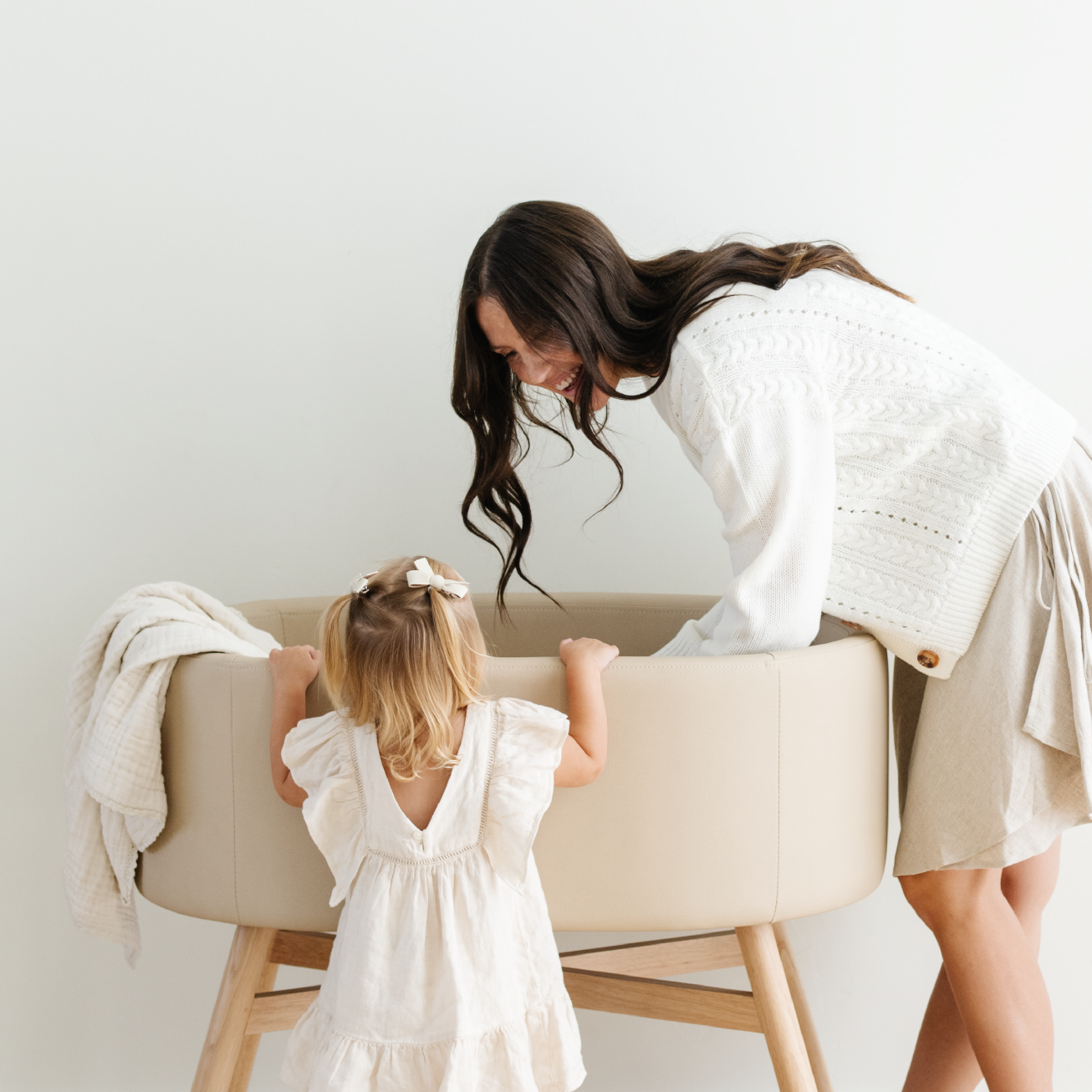 Mom and kid looking into the Gathre x babyletto Capsule Bassinet.