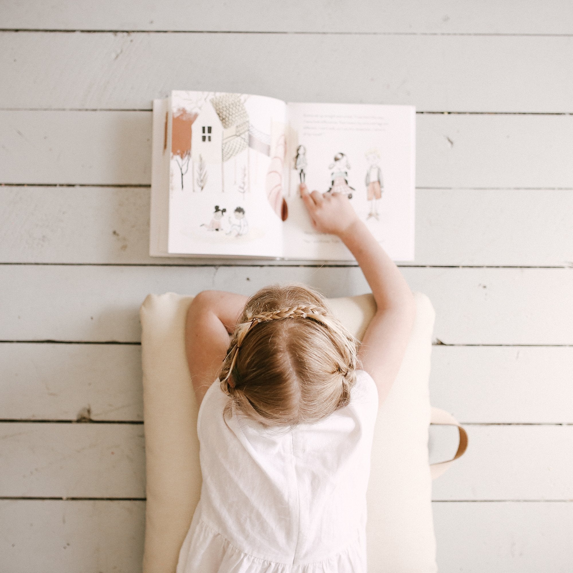 Blanc (on sale) / Square@Overhead of kid laying on the Blanc Square Mini Floor Cushion reading a book