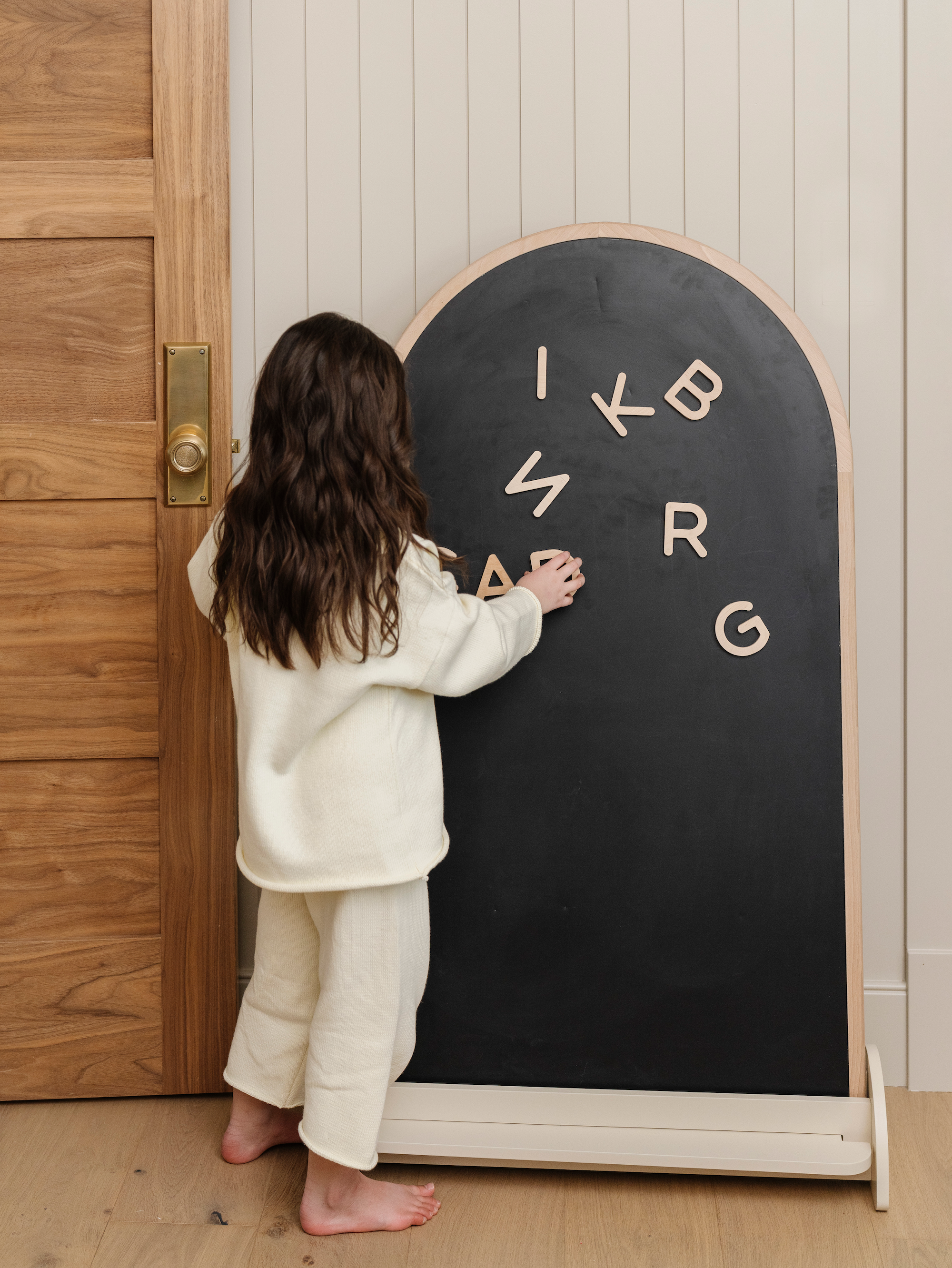 Kid playing with Wooden Letters on the Arched Chalkboard in a bedroom